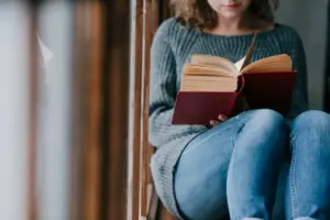Mulher lendo um livro vermelho, sentada em um banco, com foco em suas mãos e no livro aberto, simbolizando a leitura como uma forma de enfrentamento da depressão.