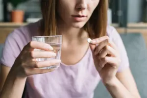 Mulher segura um copo de água e uma pílula de venlafaxina, antidepressivo usado no tratamento de depressão e ansiedade.