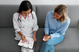 Médica orienta paciente sobre exames femininos, mostrando ilustração do sistema reprodutor em prancheta durante consulta.
