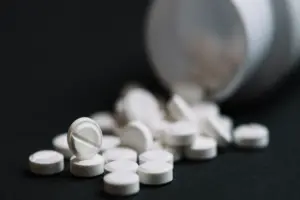 Comprimidos brancos de diazepam espalhados em uma superfície escura ao lado de um frasco. O diazepam é um medicamento ansiolítico e sedativo da classe dos benzodiazepínicos usado para tratar ansiedade intensa, espasmos musculares e insônia. É um medicamento de tarja preta devido ao risco de dependência e deve ser usado sob supervisão médica.