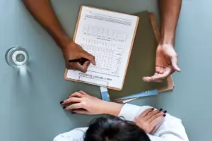 Visão de cima de duas pessoas em uma mesa, revisando um relatório médico com dados em tabela, com uma mão apontando para o documento, simbolizando a discussão dos resultados de painel genético e a prevenção personalizada do Teste Multicâncer Total.