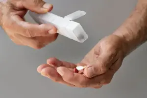 Pessoa segurando porta-comprimidos aberto e alguns comprimidos na palma da mão.