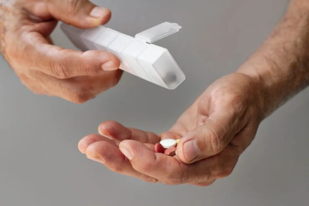 Pessoa segurando porta-comprimidos aberto e alguns comprimidos na palma da mão.