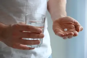 Imagem de pessoa segurando uma cápsula e um copo de água, representando o uso do medicamento e explicando para que serve dutasterida.