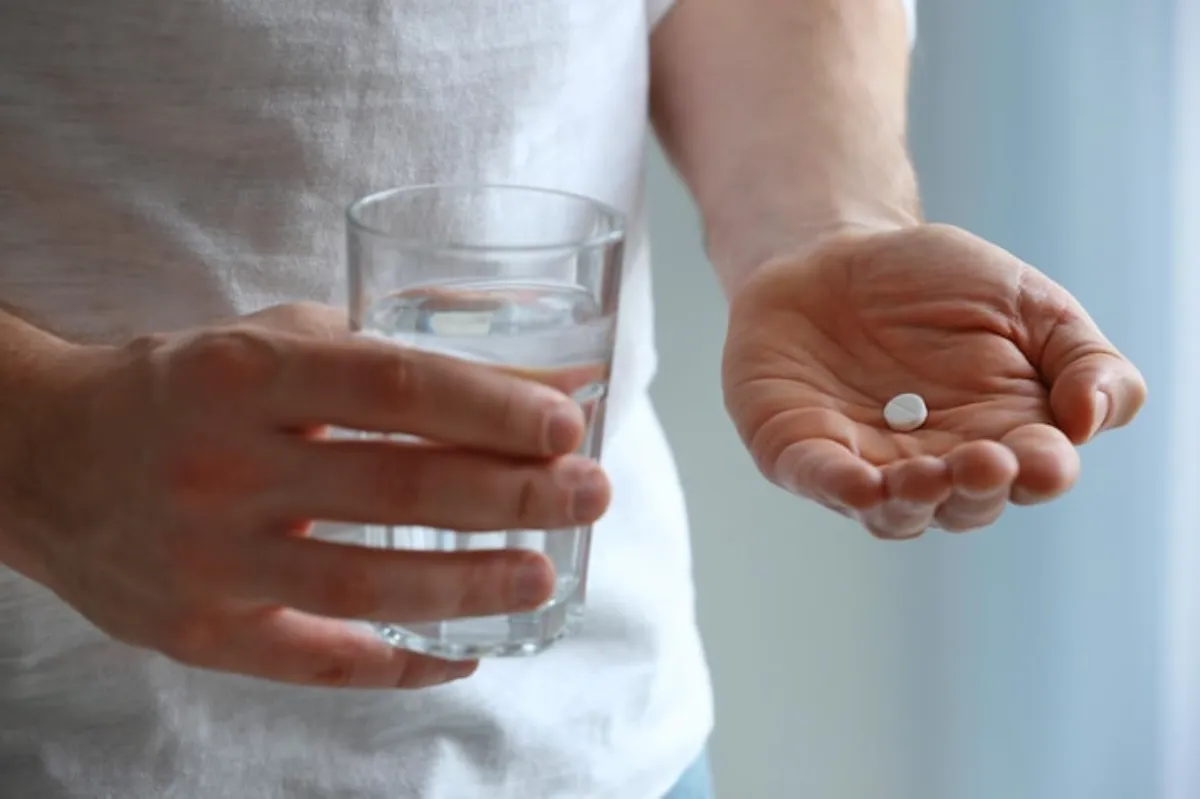 Imagem de pessoa segurando uma cápsula e um copo de água, representando o uso do medicamento e explicando para que serve dutasterida.